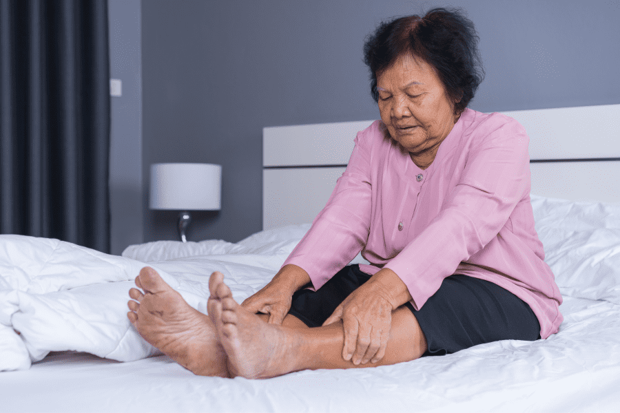 older woman laying on bed stretching forward over to grab her shins
