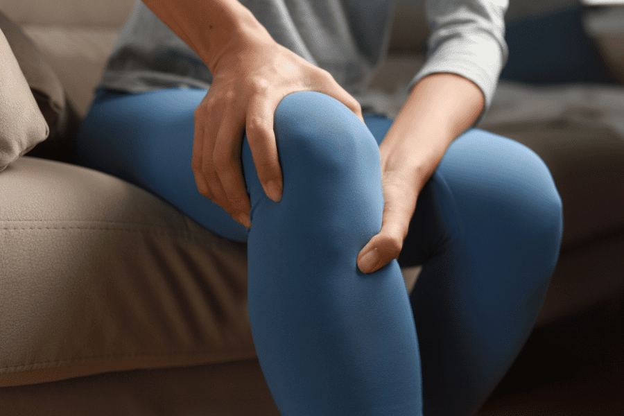 person in leggings sitting on couch holding knee in pain 
